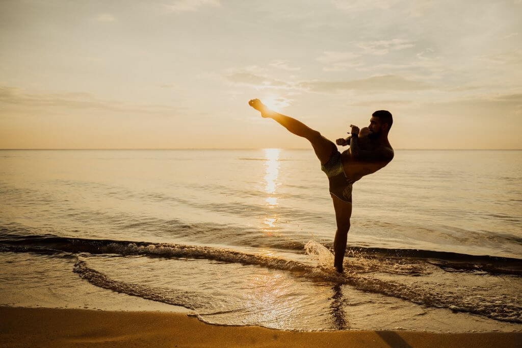 a man practicing kick boxing while on the seashore